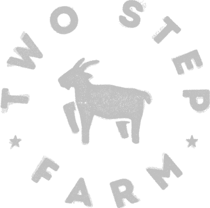 Gray silhouette of a goat in the center, surrounded by the words "Two Step Farm" in a circular arrangement with two stars at the bottom—celebrating TX at Two Step Farm.